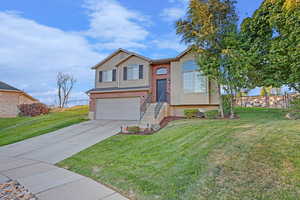 Bi-level home featuring driveway, an attached garage, a front yard, and brick siding