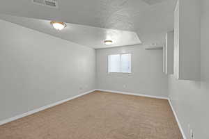 Carpeted empty room with a textured ceiling, visible vents, and baseboards