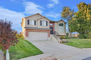 Raised ranch featuring driveway, an attached garage, a front lawn, and brick siding