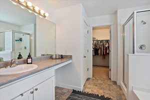 Bathroom featuring a spacious closet, a stall shower, vanity, and baseboards