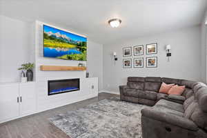 Living area featuring baseboards, dark wood-style flooring, and a glass covered electric fireplace