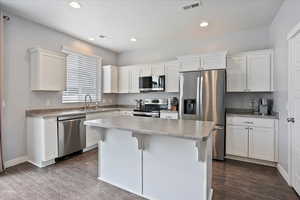 Kitchen, dark wood finished floors, appliances with stainless steel finishes, white cabinetry, granite countertops and a sink