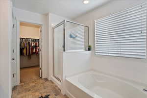 Bathroom with a garden tub, a spacious closet, stone finish floor, and a shower stall