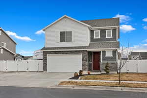 View of front of home with stone siding, a shingled roof, concrete driveway, and a gate