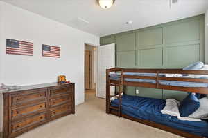 Bedroom with light carpet, a decorative wall, and visible vents