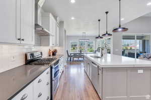 Kitchen with a center island with sink, backsplash, stainless steel appliances, wall chimney range hood, and a sink