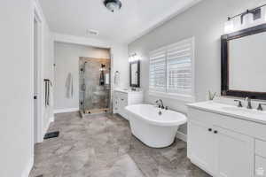 Full bath with two vanities, a sink, visible vents, a freestanding bath, and a stall shower