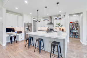 Kitchen featuring a breakfast bar area, light wood-style flooring, a sink, wall chimney range hood, and stainless steel fridge