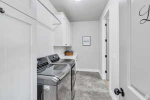 Laundry room featuring washer and dryer, marble finish floor, cabinet space, and baseboards