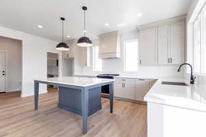 Kitchen featuring a sink, light countertops, custom exhaust hood, light wood finished floors, and gas stove