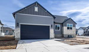 View of front of home with concrete driveway, a shingled roof, board and batten siding, and stone siding