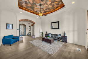 Living area featuring arched walkways, a tray ceiling, wood finished floors, and visible vents