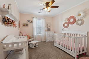 Bedroom featuring carpet floors, visible vents, ornamental molding, and a crib