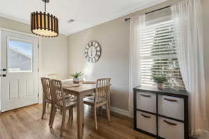 Dining space with ornamental molding, visible vents, baseboards, and wood finished floors