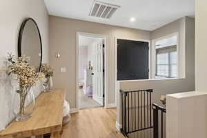 Hall with wood finished floors, an upstairs landing, visible vents, and baseboards