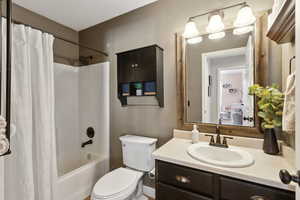 Bathroom featuring toilet, shower / bathtub combination with curtain, and vanity