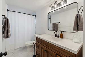 Bathroom with toilet, curtained shower, and vanity