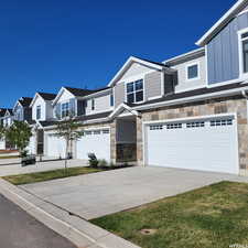 View of property featuring a residential view, stone siding, an attached garage, and concrete driveway