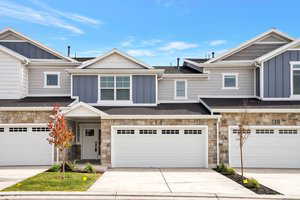 Multi unit property featuring board and batten siding, stone siding, driveway, and an attached garage