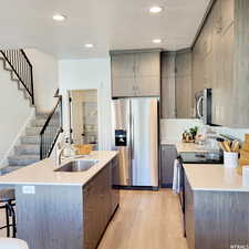 Kitchen featuring a breakfast bar, stainless steel appliances, light countertops, a sink, and light wood-type flooring