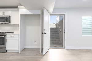 Kitchen with light wood finished floors, appliances with stainless steel finishes, white cabinetry, and baseboards