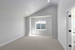 Spare room with vaulted ceiling, light carpet, and baseboards