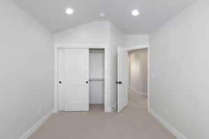 Unfurnished bedroom with baseboards, lofted ceiling, and light colored carpet