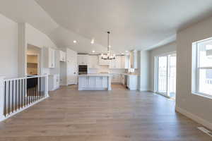 Kitchen with a center island, an inviting chandelier, appliances with stainless steel finishes, light wood-type flooring, and baseboards