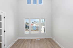 Spare room featuring visible vents, a high ceiling, light wood-style flooring, and baseboards