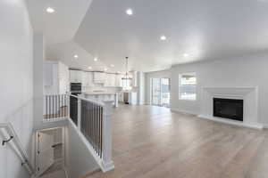 Unfurnished living room with baseboards, a glass covered fireplace, lofted ceiling, light wood-style flooring, and recessed lighting