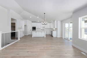 Kitchen featuring lofted ceiling, light wood-style flooring, white cabinetry, appliances with stainless steel finishes, and an inviting chandelier