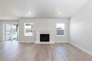 Unfurnished living room with light wood-style flooring, baseboards, and a wealth of natural light