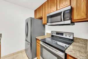 Kitchen featuring stainless steel appliances, travertine tile, and granite countertops.