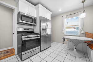 Kitchen with light tile patterned floors, baseboards, appliances with stainless steel finishes, white cabinetry, and pendant lighting