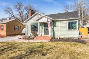 Bungalow featuring a shingled roof, a front yard, fence, and a chimney