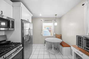 Kitchen featuring light tile patterned floors, baseboards, white cabinets, hanging light fixtures, and stainless steel appliances