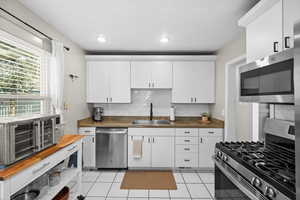 Kitchen featuring decorative backsplash, appliances with stainless steel finishes, wooden counters, a sink, and light tile patterned flooring