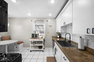 Kitchen featuring light tile patterned floors, recessed lighting, a sink, white cabinets, and backsplash