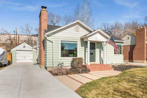 Bungalow with an outbuilding, a garage, concrete driveway, a front lawn, and a chimney