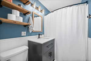 Bathroom with a shower with shower curtain, a wainscoted wall, vanity, and toilet