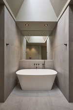 Full bath featuring lofted ceiling, a freestanding tub, and tile walls