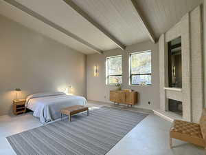 Bedroom with a brick fireplace, vaulted ceiling with beams, and finished concrete flooring