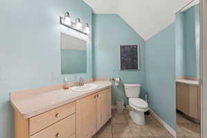 Bathroom with lofted ceiling, vanity, toilet, and tile patterned floors