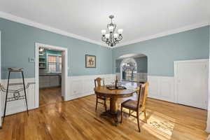 Dining space featuring arched walkways, a wainscoted wall, crown molding, light wood-style flooring, and an inviting chandelier