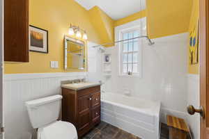 Full bath featuring toilet, a wainscoted wall, tile patterned flooring, vanity, and washtub / shower combination