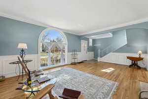 Living area featuring stairway, wainscoting, wood finished floors, and crown molding