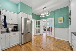 Kitchen featuring french doors, light wood-type flooring, freestanding refrigerator, decorative backsplash, and dark countertops