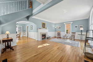 Living area with arched walkways, wood finished floors, a fireplace with flush hearth, visible vents, and ornamental molding