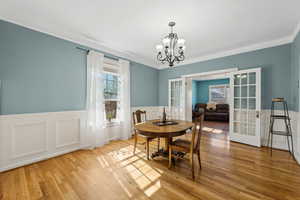 Dining space featuring french doors, crown molding, an inviting chandelier, wainscoting, and wood finished floors