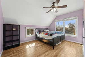 Bedroom with lofted ceiling, multiple windows, baseboards, and wood finished floors